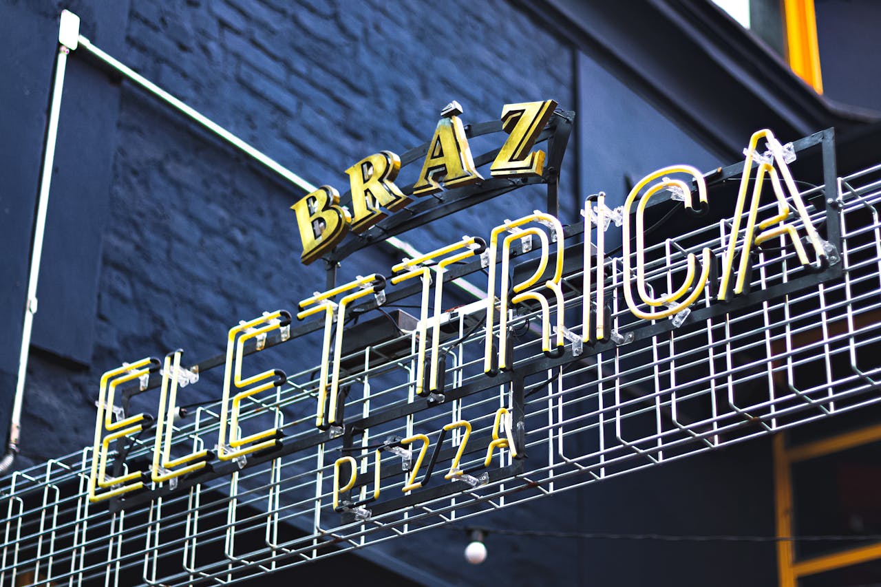 A vibrant neon sign displaying Elettrica at a pizza restaurant, captured outdoors with a striking low angle.